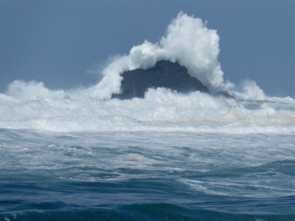 Large ocean wave breaking over coastal rocks