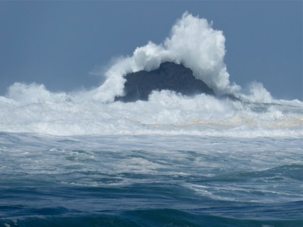 Large ocean wave breaking over coastal rocks