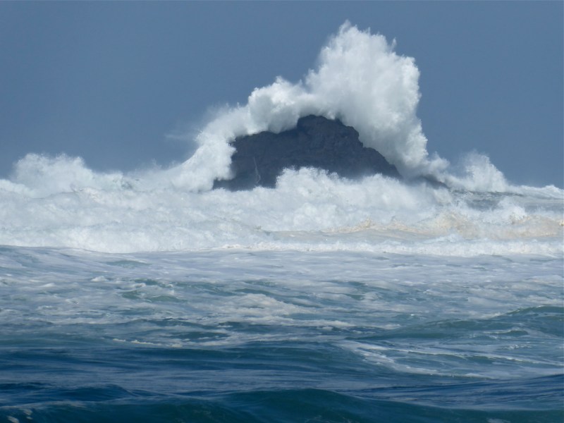Large ocean wave breaking over coastal rocks