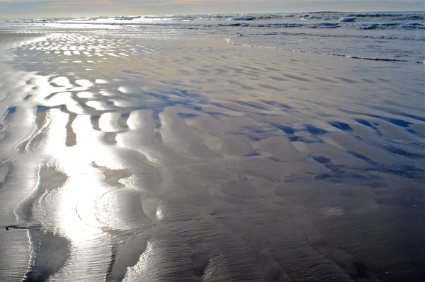 Flat, sandy beach with blue-sky reflected in runnels and surf in distance