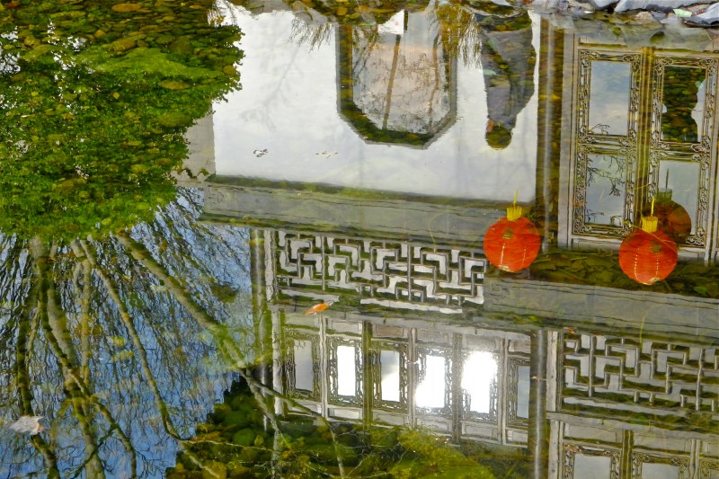 Reflection of teahouse, trees and passerby in garden pool