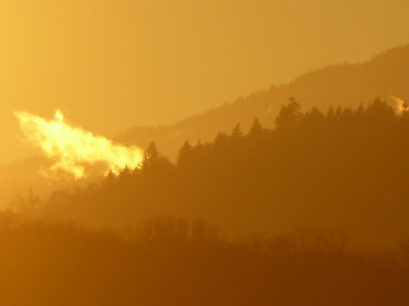 Yellowish sky and cloud over hazy, forested ridges
