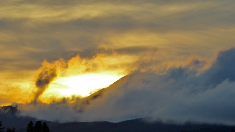 Sun setting in cloudy sky over mountain ridge wrapped in clouds