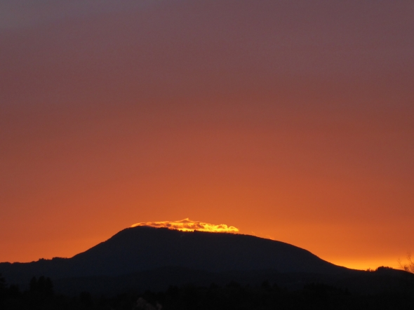 Low mountain silhouetted against orang sky after sunset