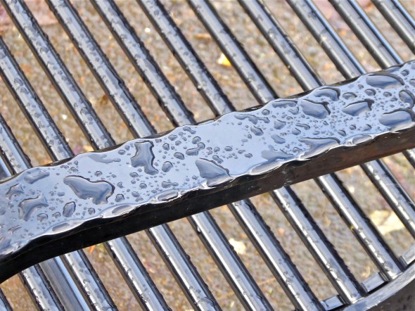 Raindrops on diagonal slats and arm of black metal park bench bl