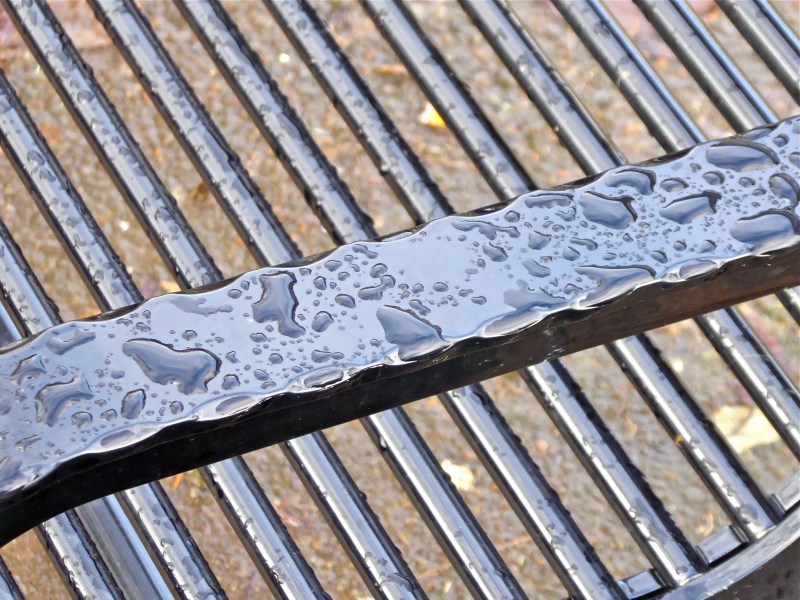 Raindrops on diagonal slats and arm of black metal park bench bl