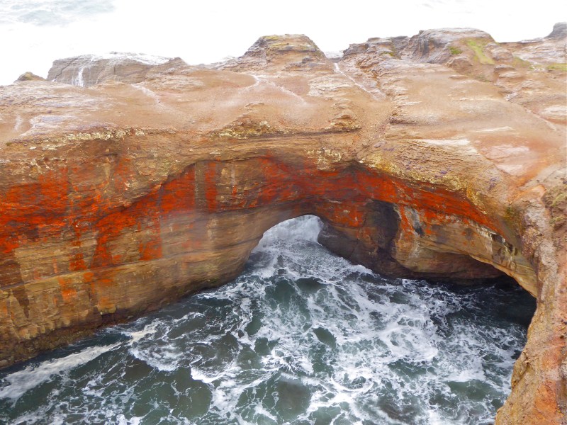 Tan and orange sea cliffs with foaming ocean surging through rocky archway