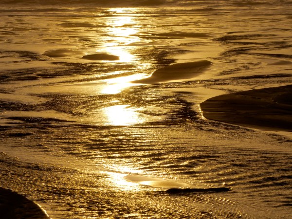 Sunlight reflected in shallow runnels on golden sandy beach