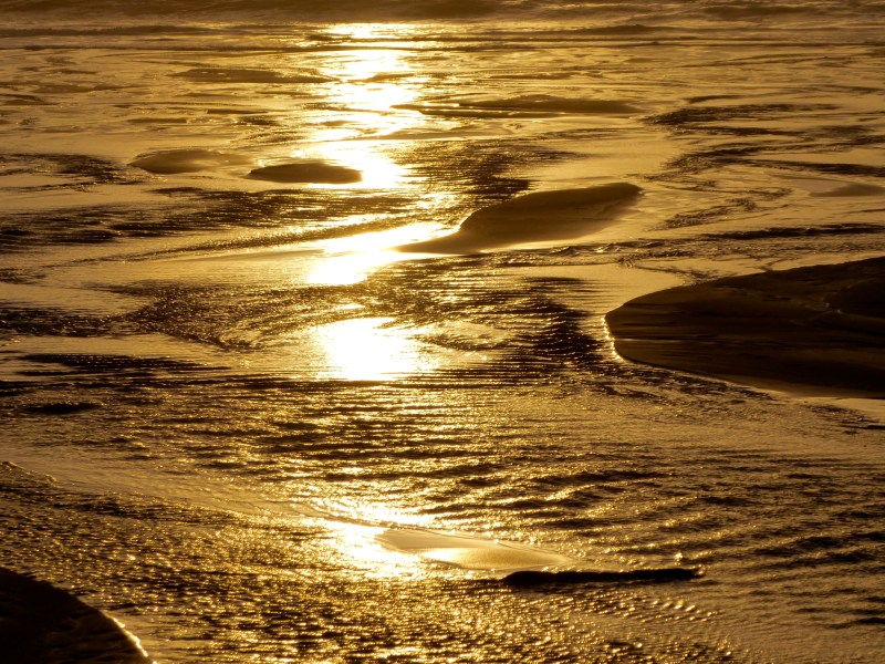 Sunlight reflected in shallow runnels on golden sandy beach