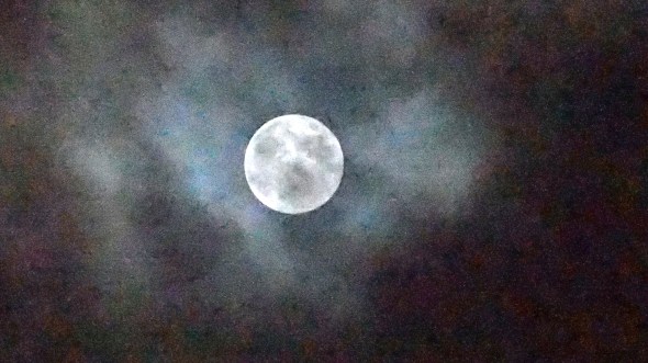 Full Moon partly shrouded by clouds in colorful dark sky