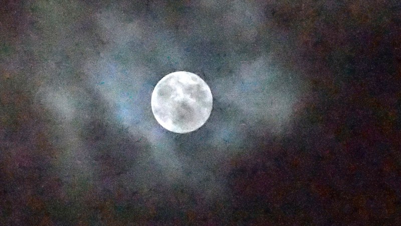 Full Moon partly shrouded by clouds in colorful dark sky