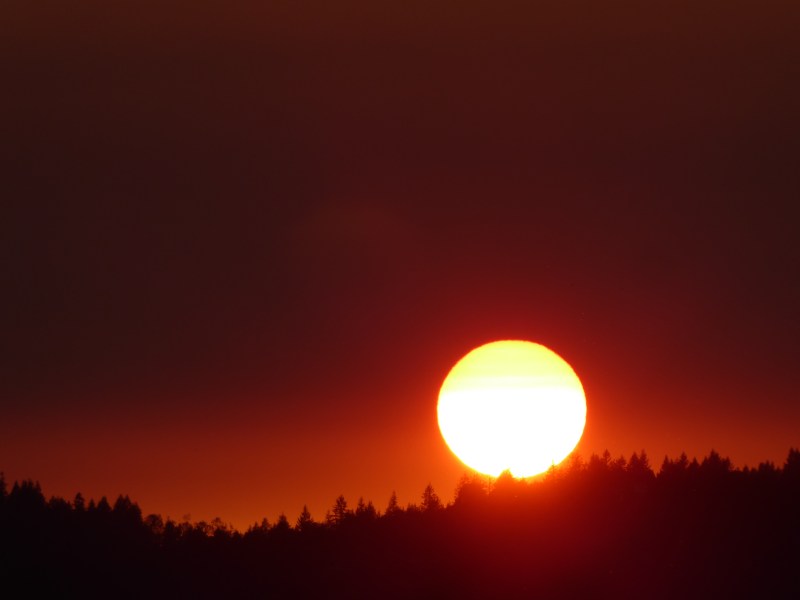 Deep orange sky and yellow sun setting over forested horizon