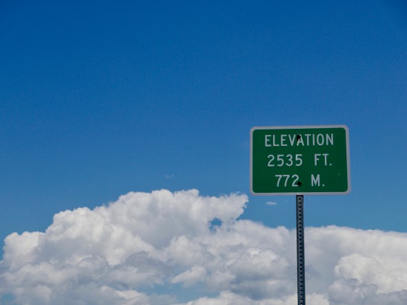 Elevation sign with blue sky and white puffy clouds