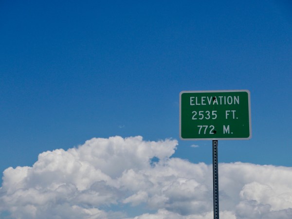 Elevation sign with blue sky and white puffy clouds
