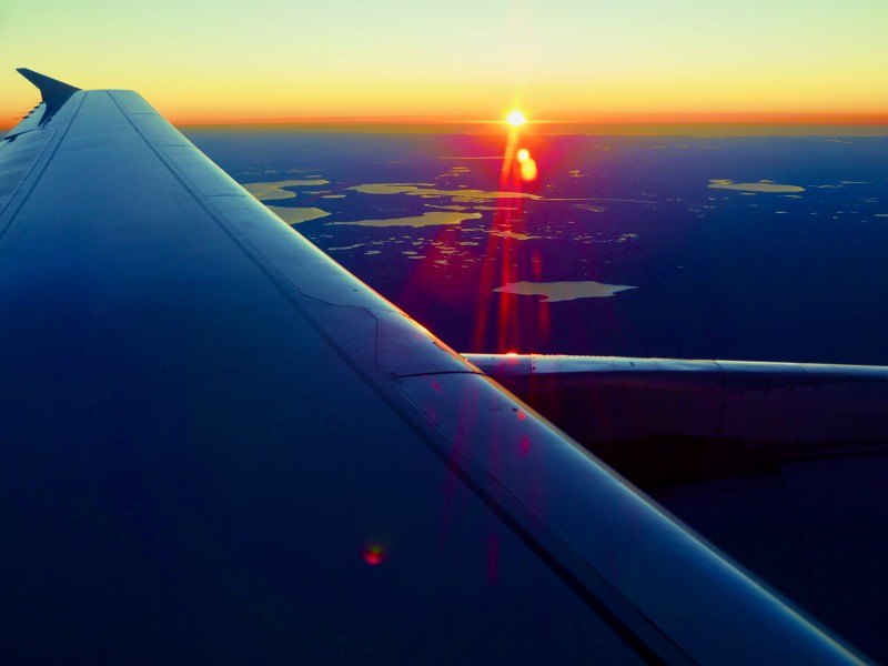 Airplane wing and setting sun over flat Florida landscape with many lakes