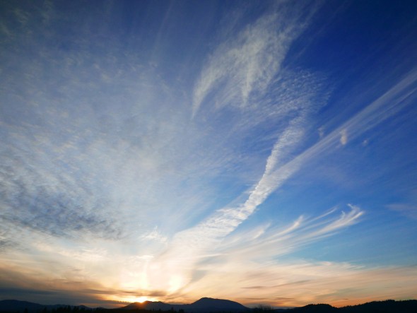 Setting sun over mountains with high clouds and blue sky