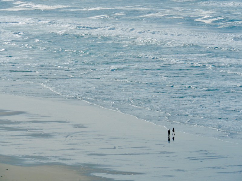 Two people walking next to blue ocean surf