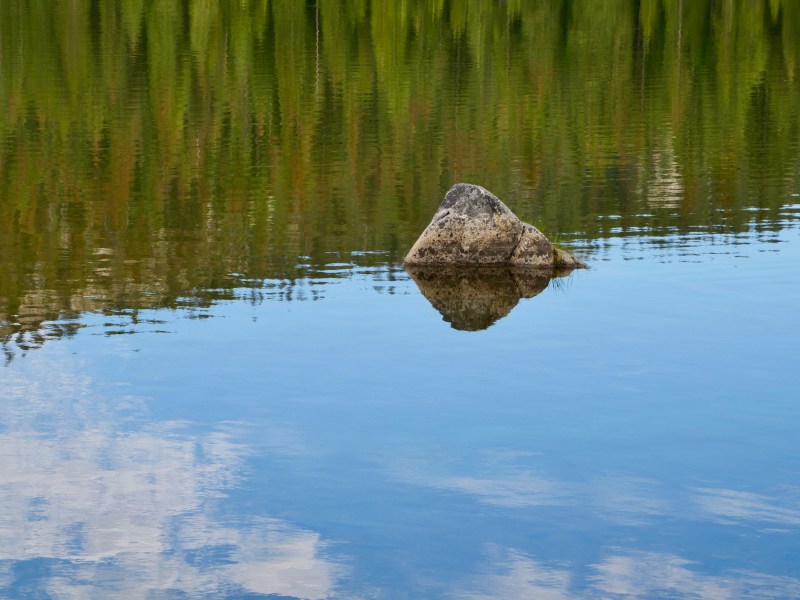Rock in lake with reflections of trees and sky