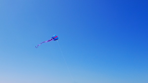 Blue and red kite with purple tail soaring in blue sky