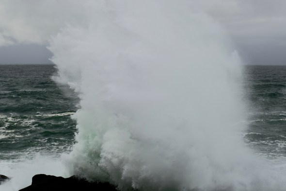 Spray high in air as breaking wave hits rocky coastline