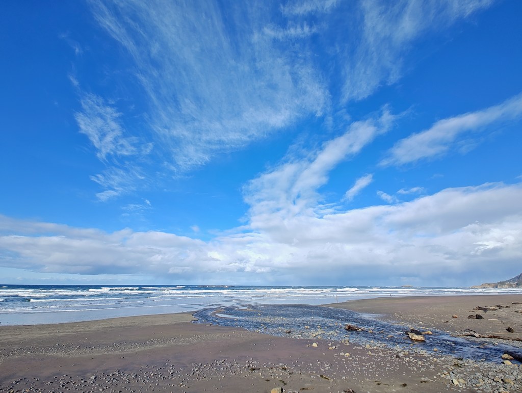 wide-angle view of surf, sandy beach and blue sky with white clouds