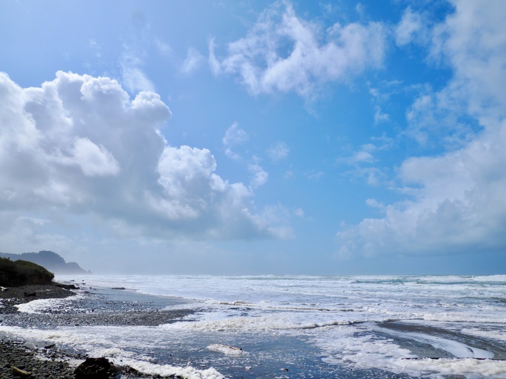 beach, surf, beach and coastal headlands with blue sky and big, puffy clouds overhead