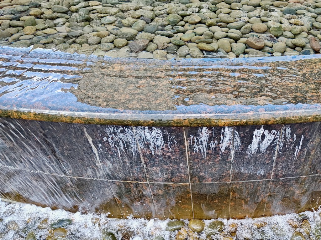fountain with falling water, reflections and pebbles