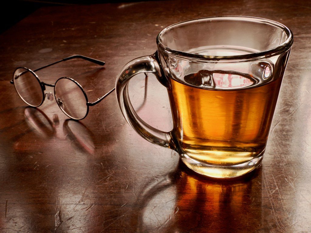 glass of amber tea and round eyeglasses on worn wooden table
